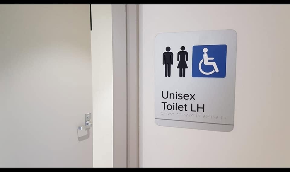 Braille and tactile unisex accessible toilet sign fitted beside a door