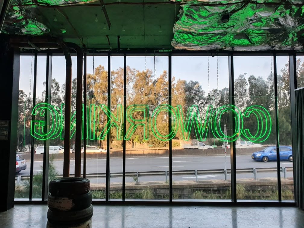 1.5 by 7 metre indoor neon lettering on clear acrylic backing, chain-hung behind a full-height window