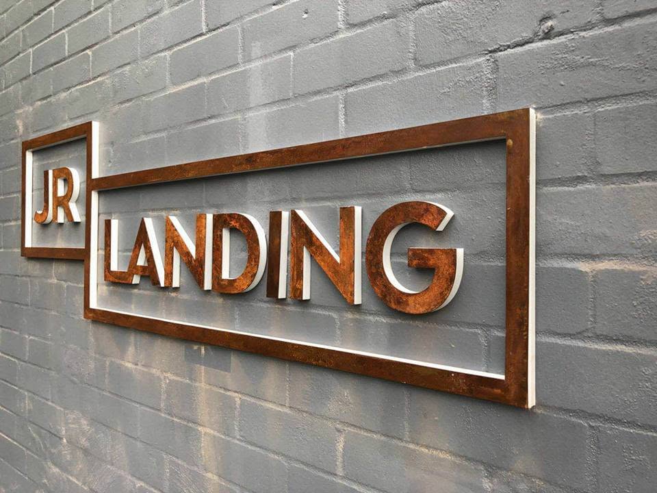 Rusted corten steel letters and frame for JR Landing on painted brick