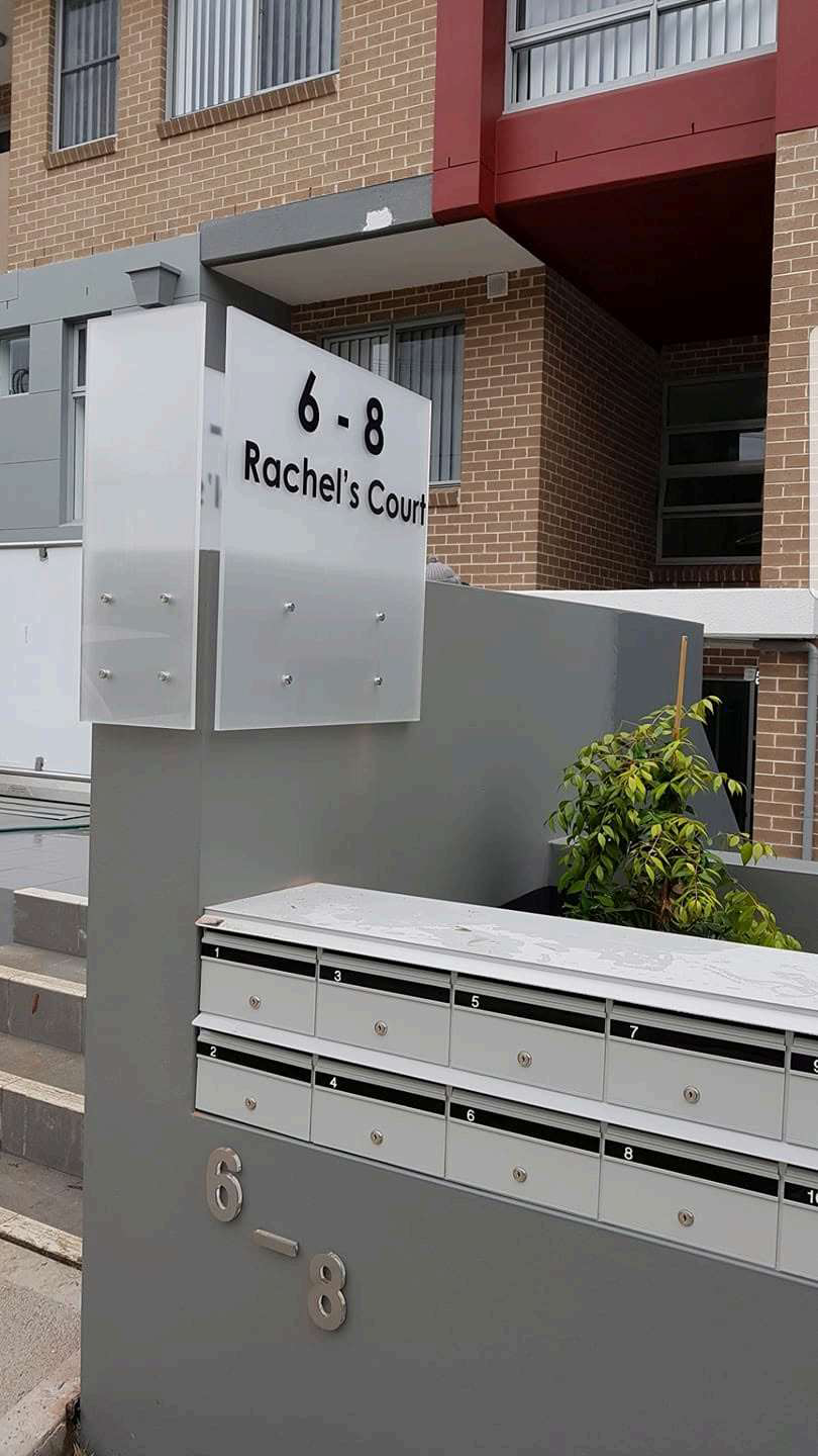 Frosted acrylic entry sign on a rendered wall, residential strata block
